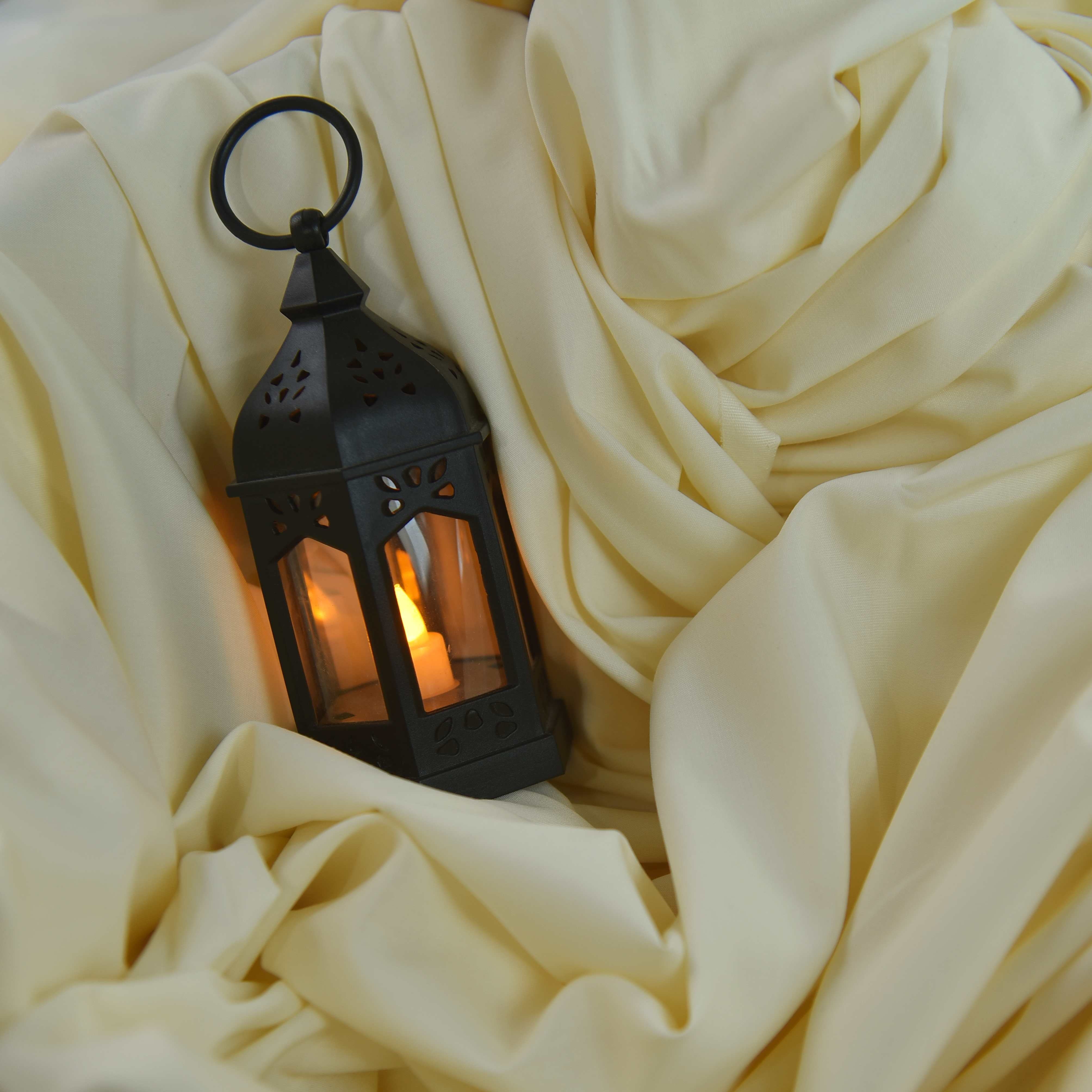 Black lantern with a glowing interior on a white fabric background