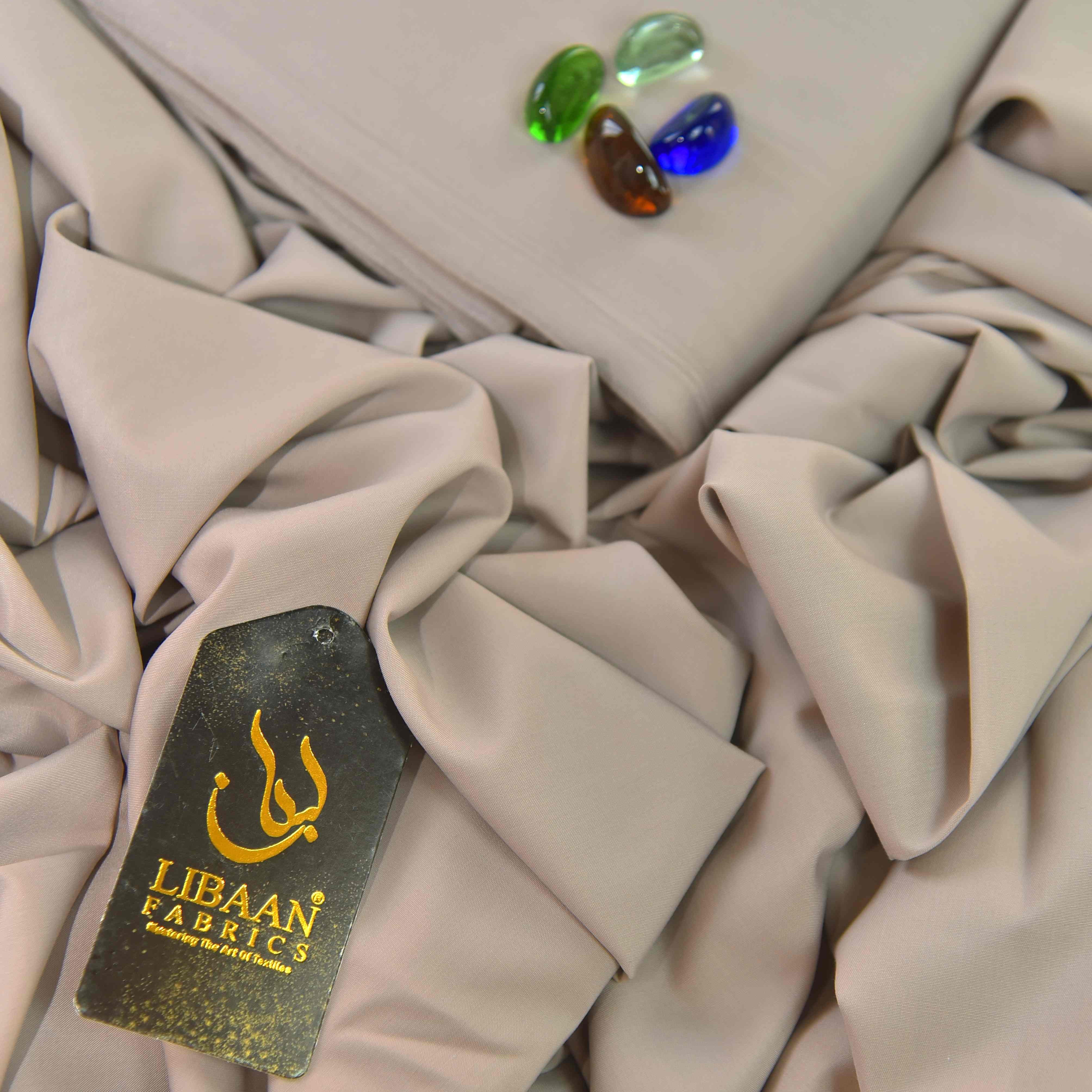Beige fabric with a Libaán Fabrics tag and colorful stones on a light gray background